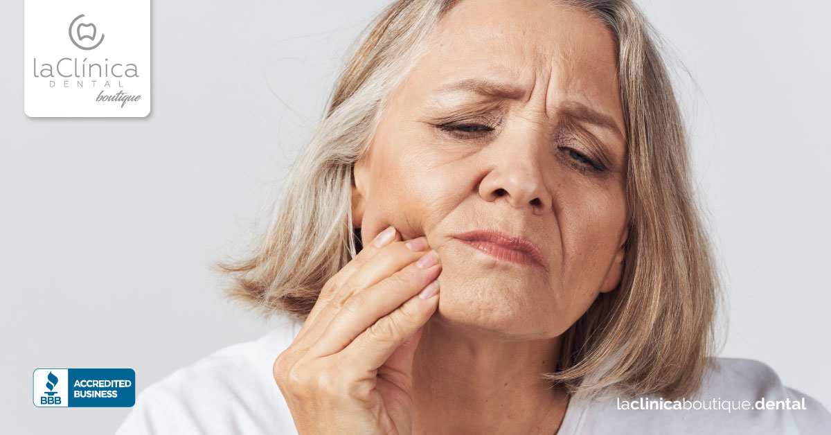Mujer con dolor dental tocándose la mejilla, mostrando incomodidad, con logotipo de La Clínica Dental Guadalajara y sello de negocio acreditado.