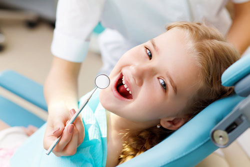 Niña sonriendo en silla dental con herramientas odontológicas, representando la odontología infantil en La Clínica Dental Guadalajara.