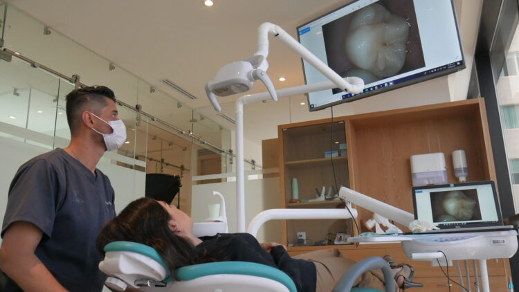 Dentista asistiendo a paciente en clínica dental moderna, con pantallas mostrando diagnóstico digital y tecnología avanzada.