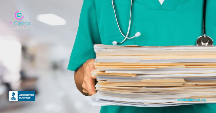Médico sosteniendo un montón de expedientes médicos dentales en un entorno clínico, destacando la atención a la salud y la seguridad en La Clínica Dental Guadalajara.