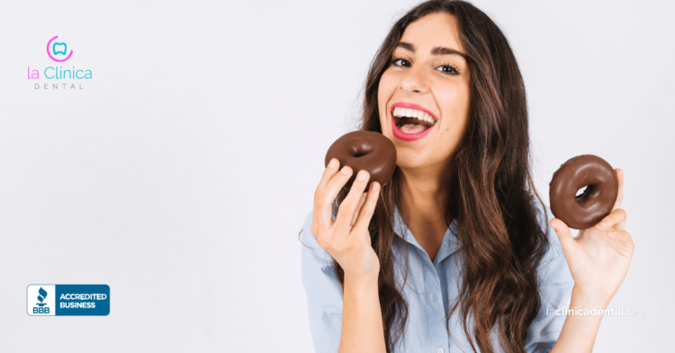 Mujer sonriendo y sosteniendo donas, destacando la importancia de la salud dental y la prevención de caries en La Clínica Dental Guadalajara.