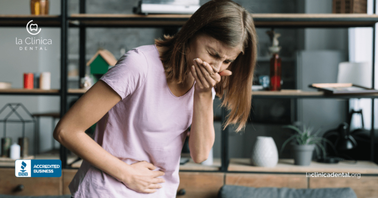 Mujer con malestar estomacal, tocándose el abdomen, representando problemas de salud relacionados con caries y su impacto en la salud dental, con el logo de La Clínica Dental Guadalajara.