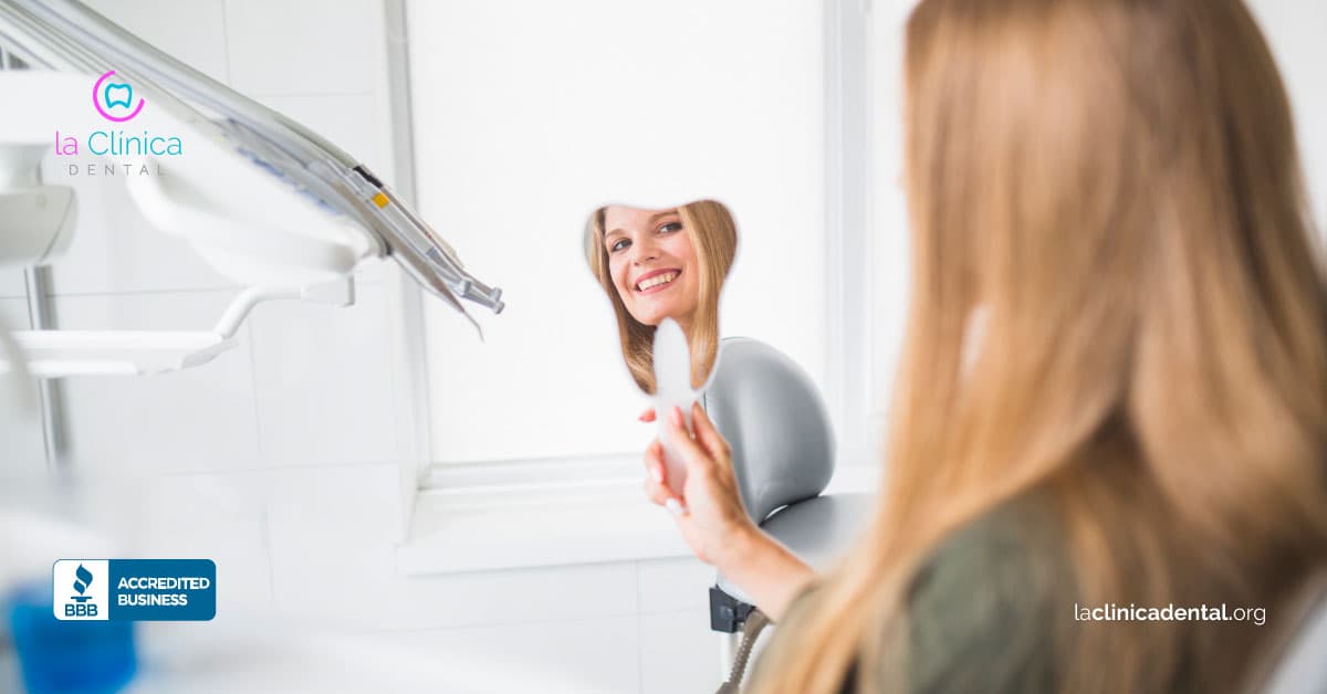 Mujer sonriendo mientras se mira en un espejo en la clínica dental, destacando la importancia de la salud dental y la atención en La Clínica Dental Guadalajara.