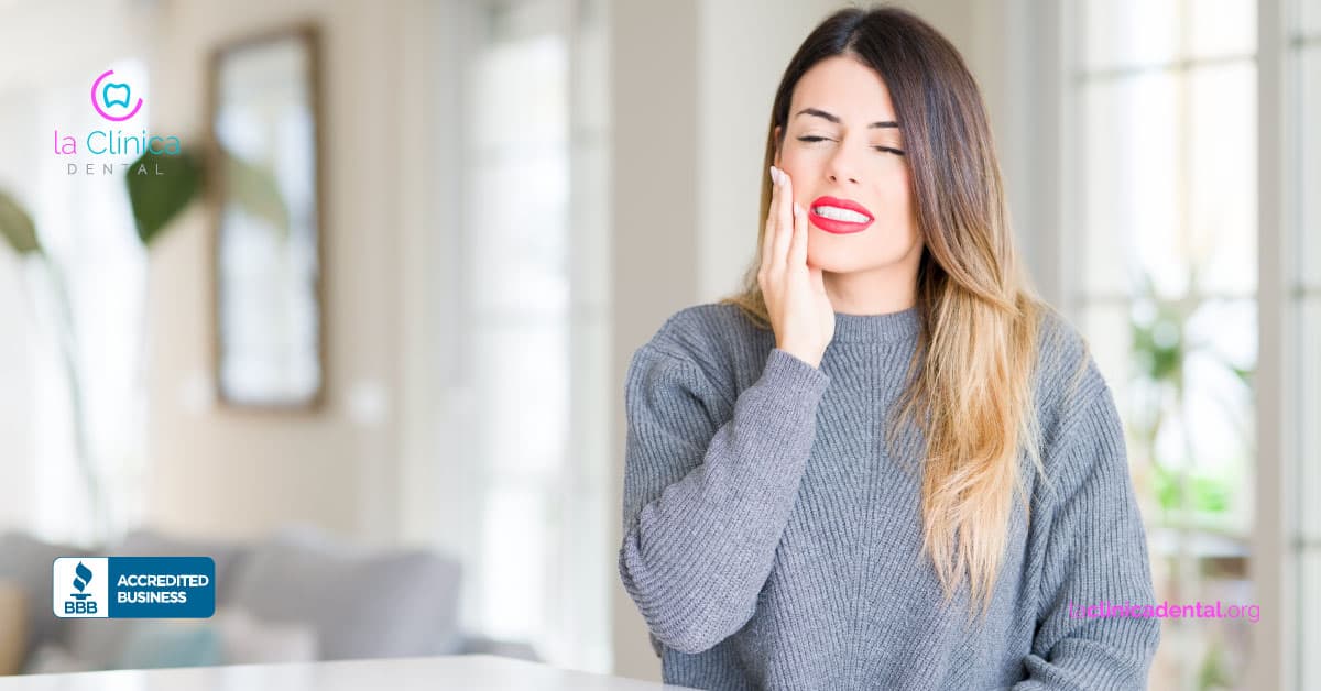 Mujer con dolor dental tocándose la mejilla, representando efectos del frío en la salud dental y bruxismo, con logo de La Clínica Dental Guadalajara.