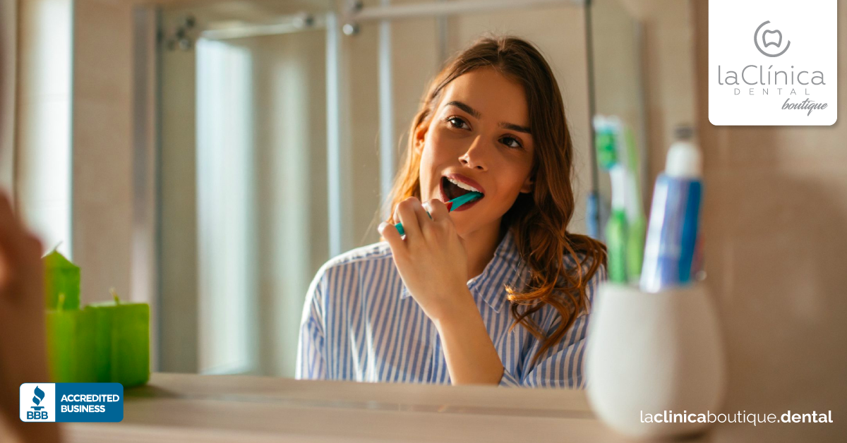 Mujer cepillándose los dientes en un baño, destacando la importancia de la higiene dental durante el verano de 2020.